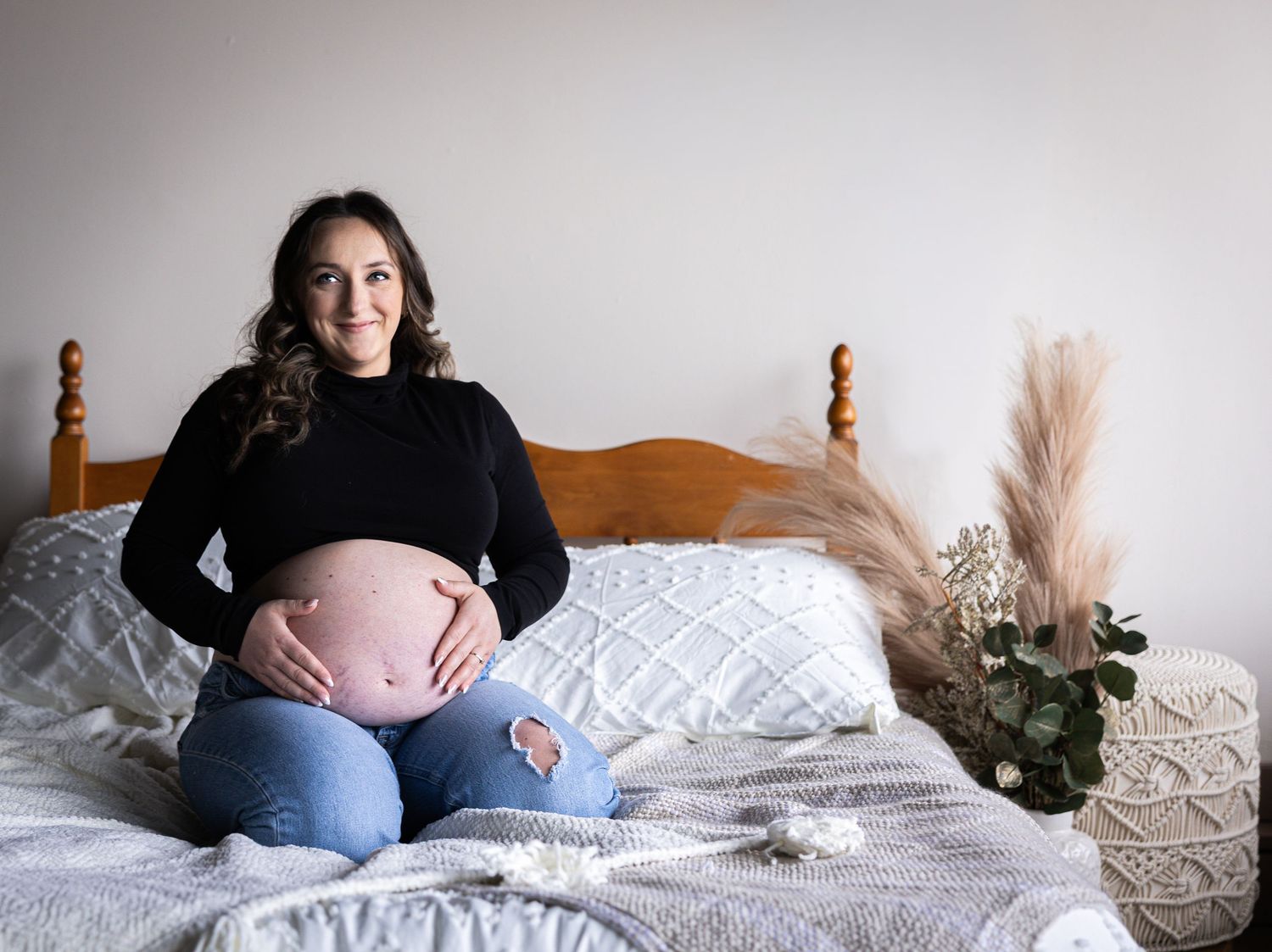 A series of pregnancy progression photos showing a growing baby bump on a bed with decorative pampas grass accents.