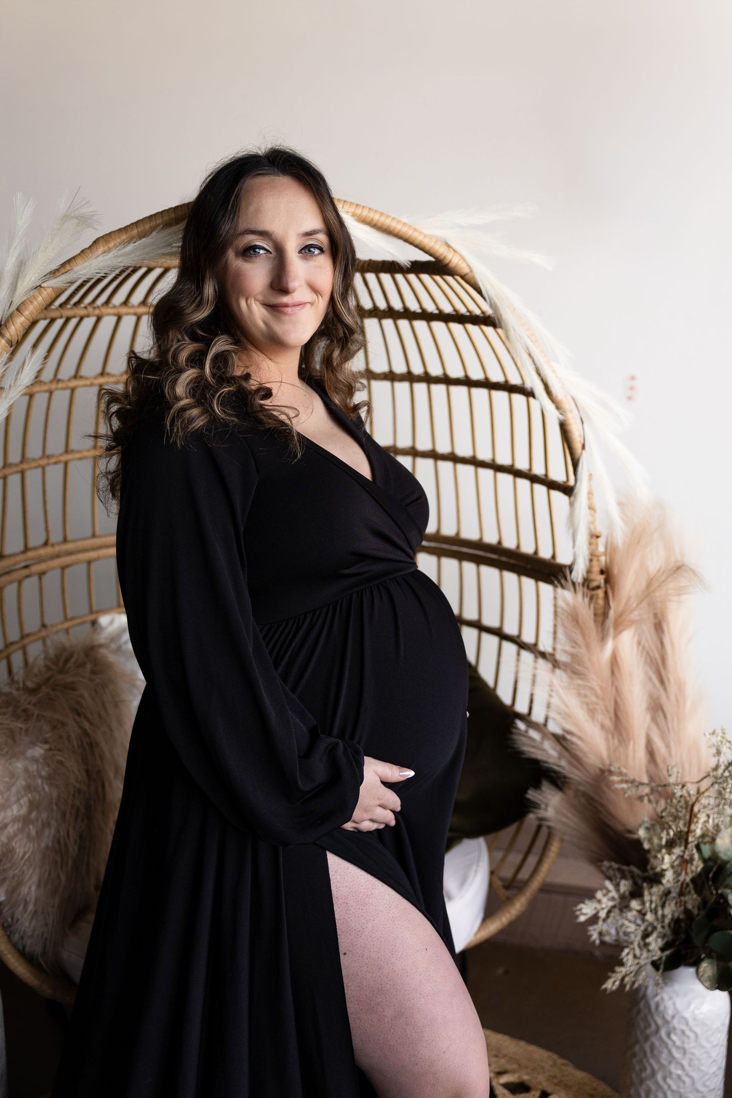 Artistic maternity photo with a flowing black dress against a light background with dried pampas grass.