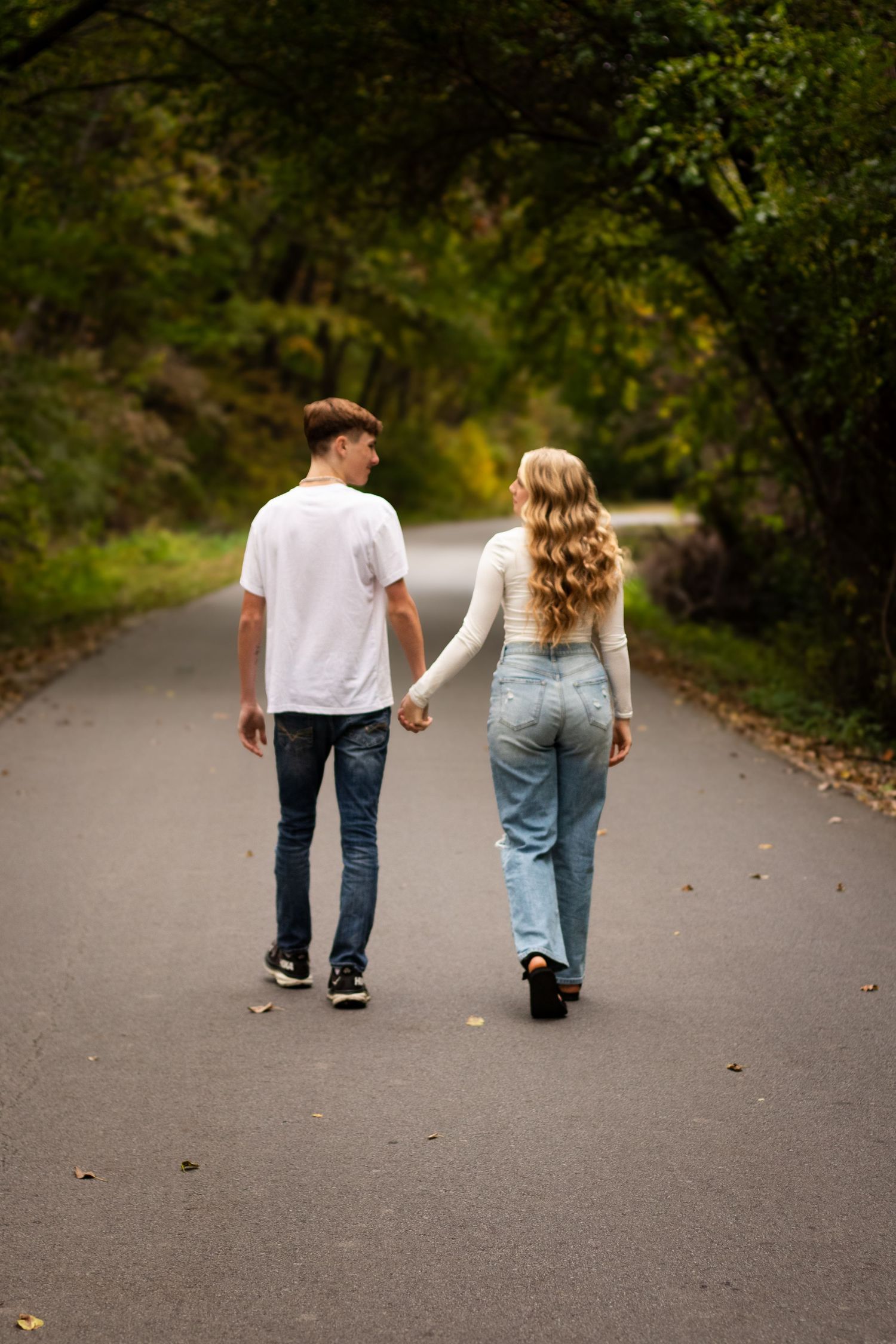 A couple walks away from the camera on a tree-lined path, shown in a series of similar shots creating a cinematic effect.