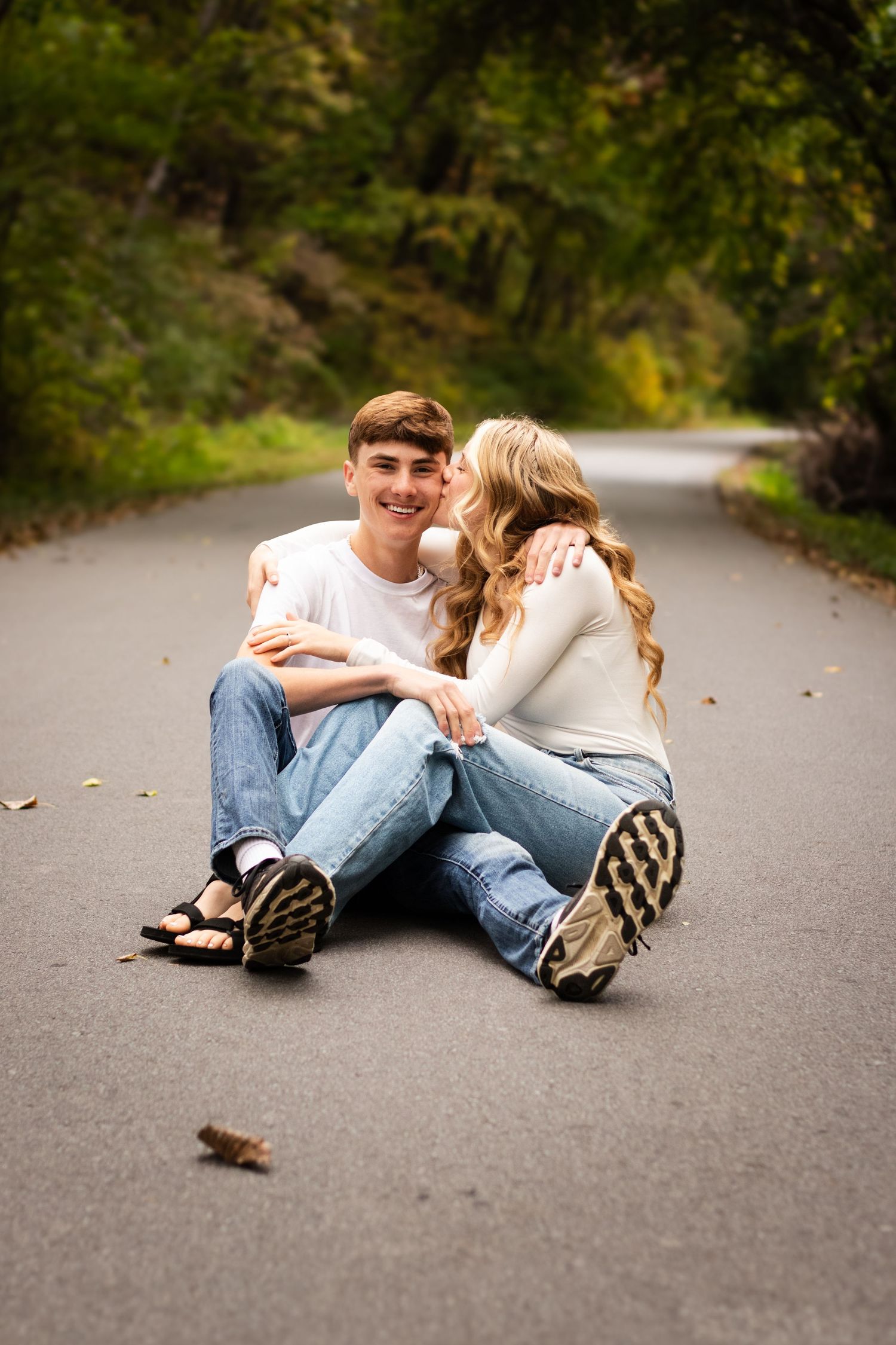 A couple relaxes together on a winding asphalt road surrounded by green trees and foliage.