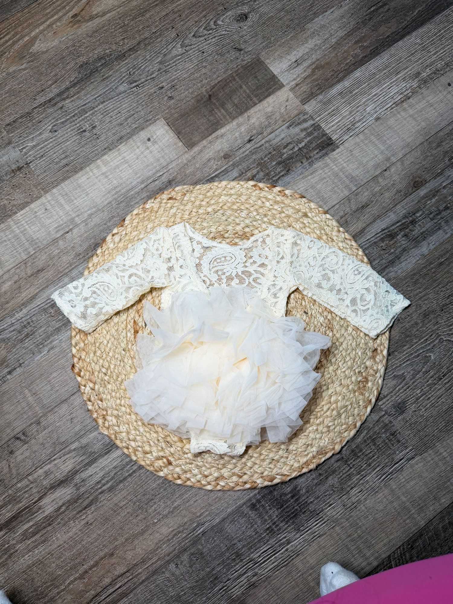 Ivory lace and tulle baby girl romper dress displayed on a woven rattan mat on wood floor.