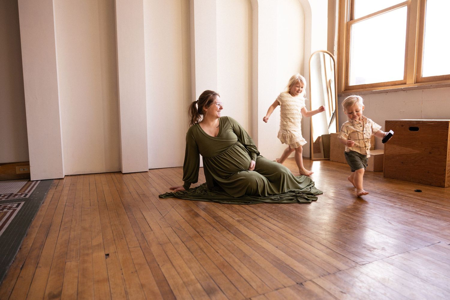 Person in green clothing lying on wooden floor near sunlit window in yoga or relaxation pose.