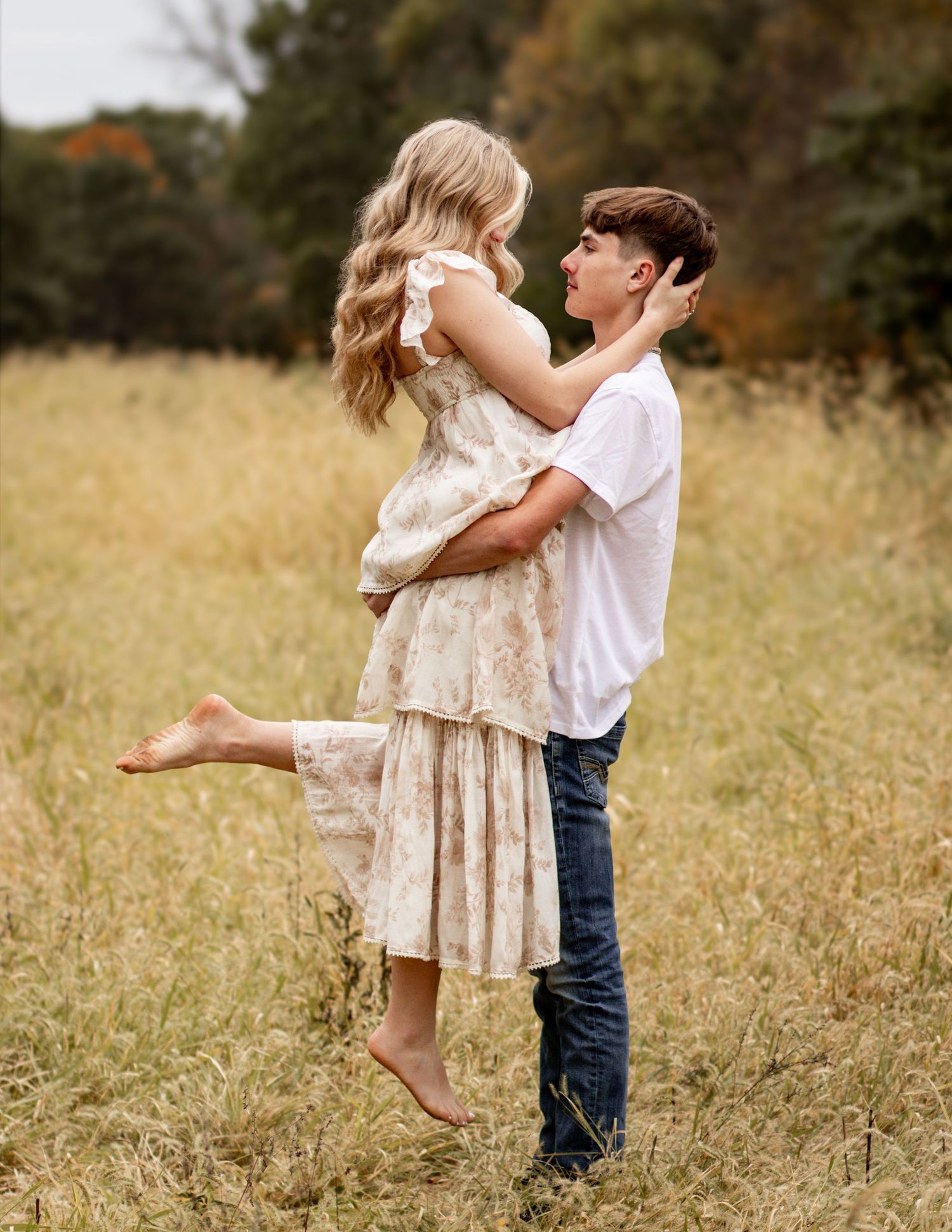 A couple in casual attire embraces playfully in a golden autumn field during a romantic photoshoot.