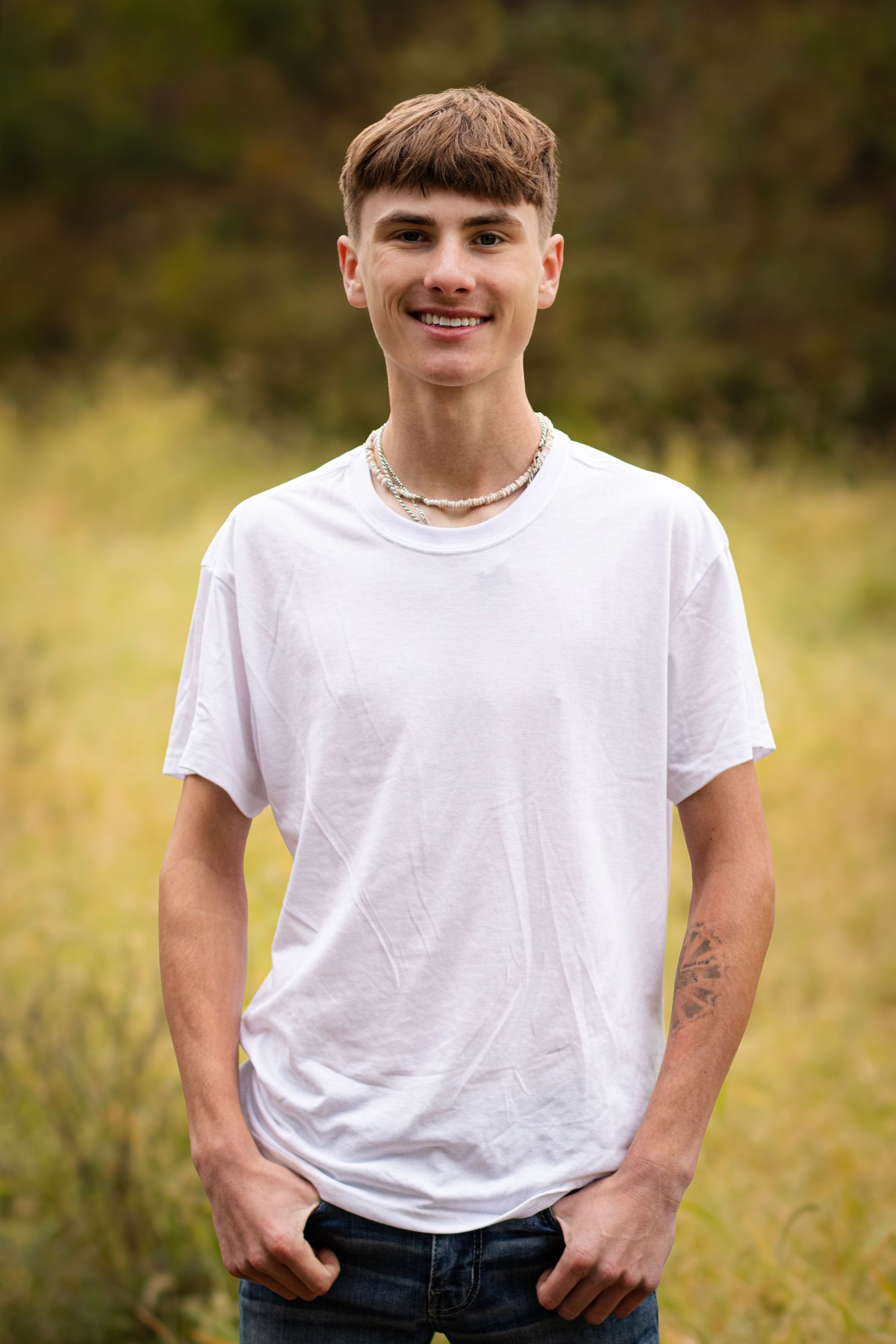 A person wearing a white t-shirt poses casually in a grassy outdoor setting with natural lighting.