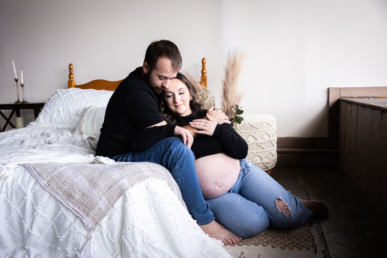 Person wearing jeans lies comfortably on white bedding while reading or using a mobile device.