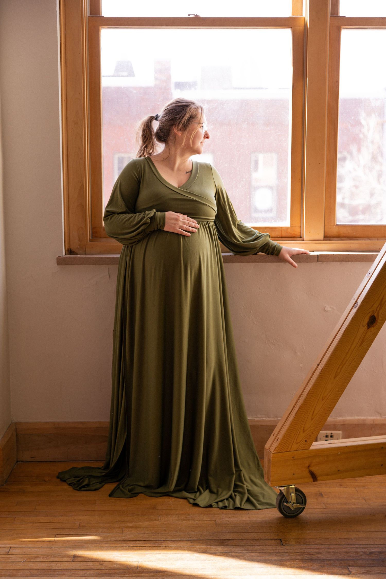 Four sequential photos of a person in a flowing olive green dress sitting by sunlit windows in a rustic wooden room.