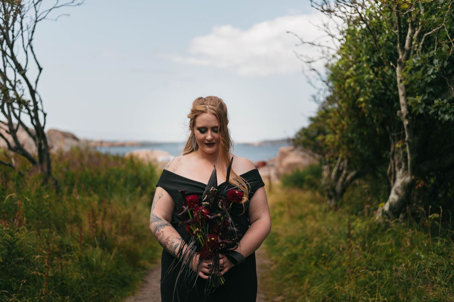 Vackert porträtt på en brud i svart brudklänning på en kuststig med havet som bakgrund i Lysekil, Bohuslän