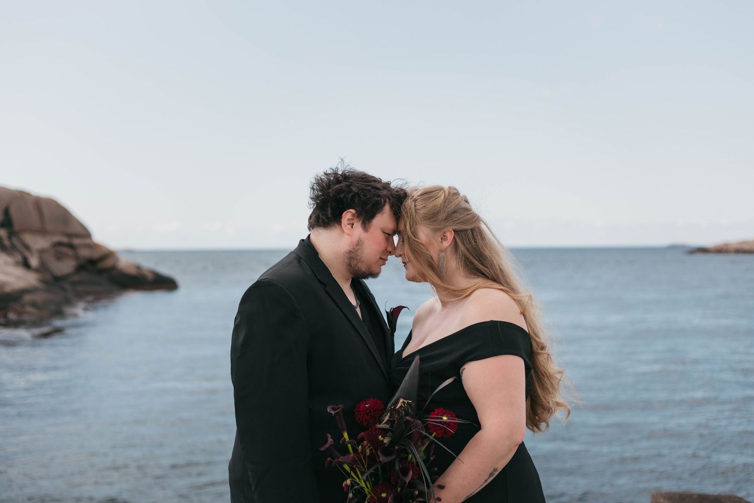 Vackert porträtt med ett brudpar klätt i svart med havet och klipporna i Lysekil, Bohuslän som bakgrund.
