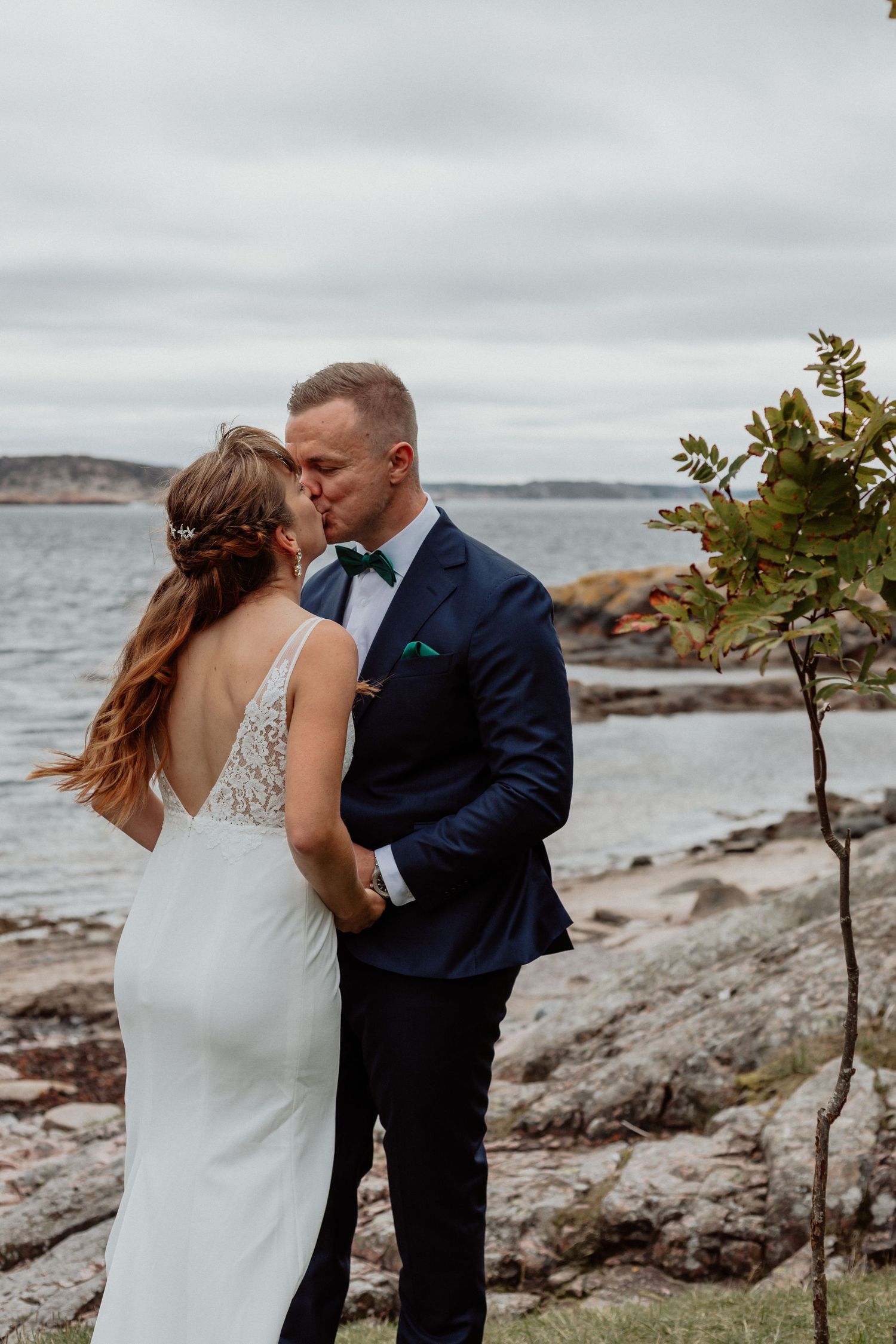 Brudpar som kysser varandra med havet och klippor i bakgrunden
