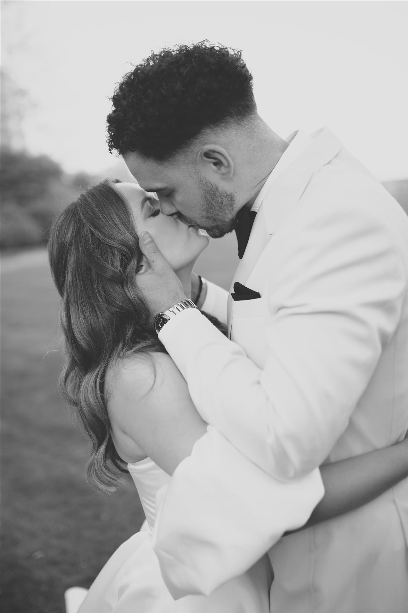A romantic black and white photo of a couple sharing an intimate kiss while embracing outdoors.