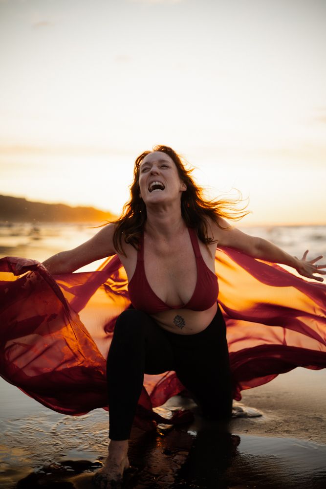 Woman expressing her frustration and anger on the beach by letting out a scream. Kneeling down into the sand.