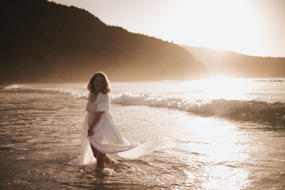 Woman in a white kimono playing in the breaking waves at sunset on the beach.