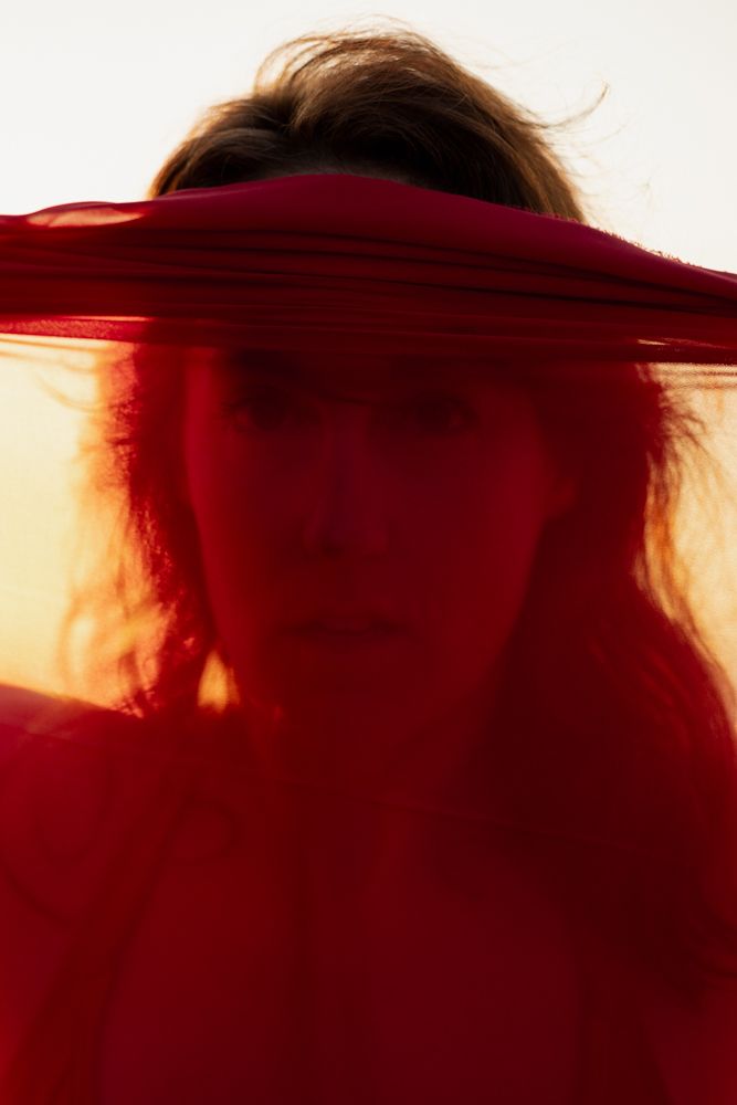Woman close up portrait looking through red see through fabric.