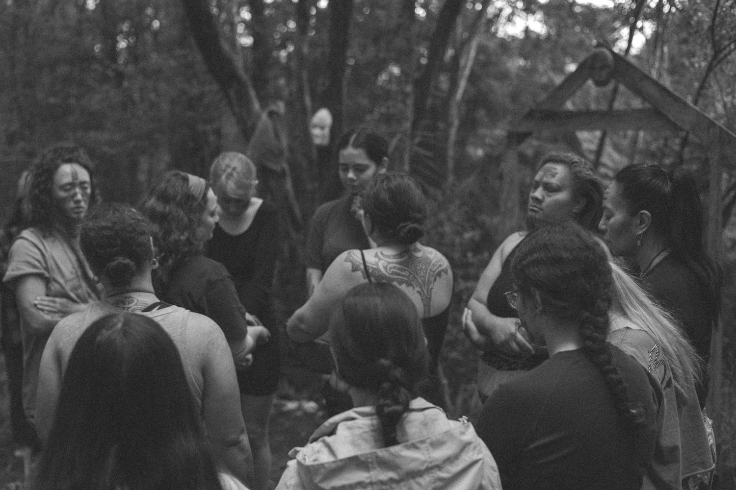 A group of woman standing in a circle, in a forest clearing with their eyes closed. One woman in the middle leading the ceremony as a rite.