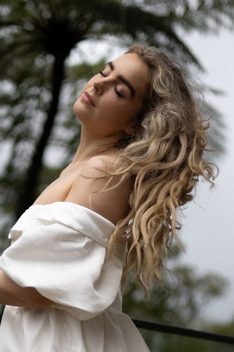 Close up of a woman in nature with a long white dress on gently shaking her long hair out symbolising breaking herself free.