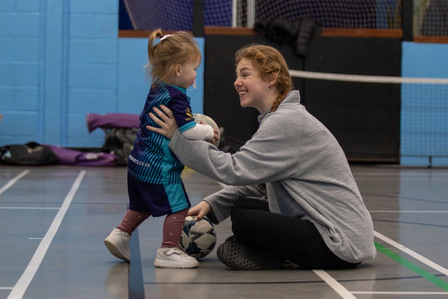 nice moment between mum and daughter, smiling at each other, sat on the floor.