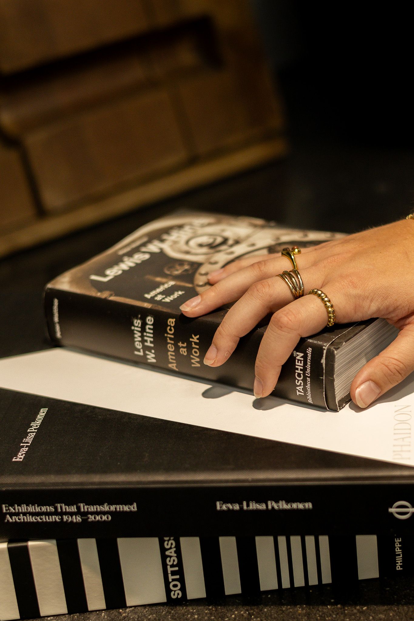A hand with gold rings rests on a Lewis Hine photography book atop architecture coffee table books by Taschen.