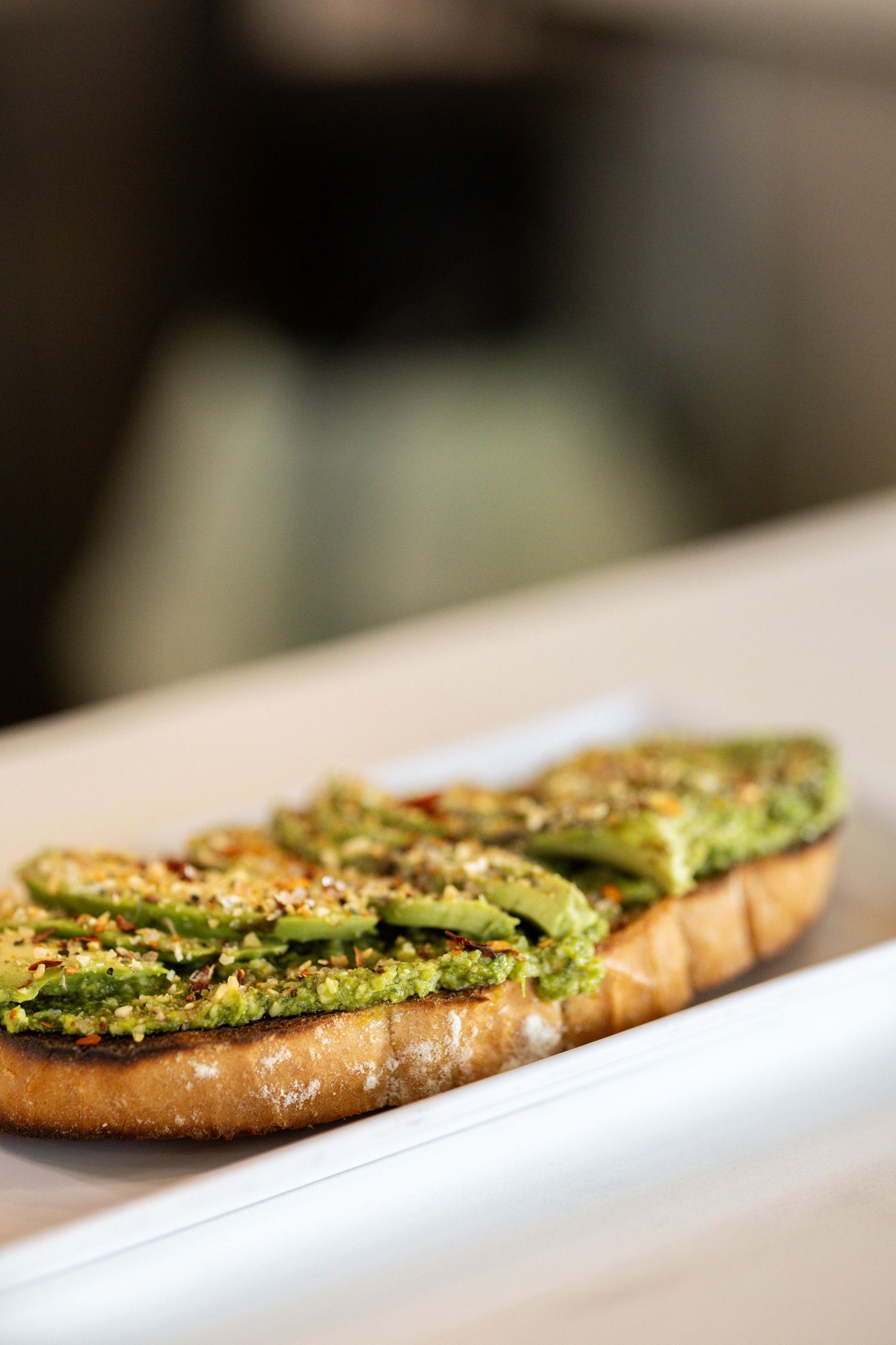 Avocado toast on crusty bread topped with seeds and seasoning, served on a white plate.