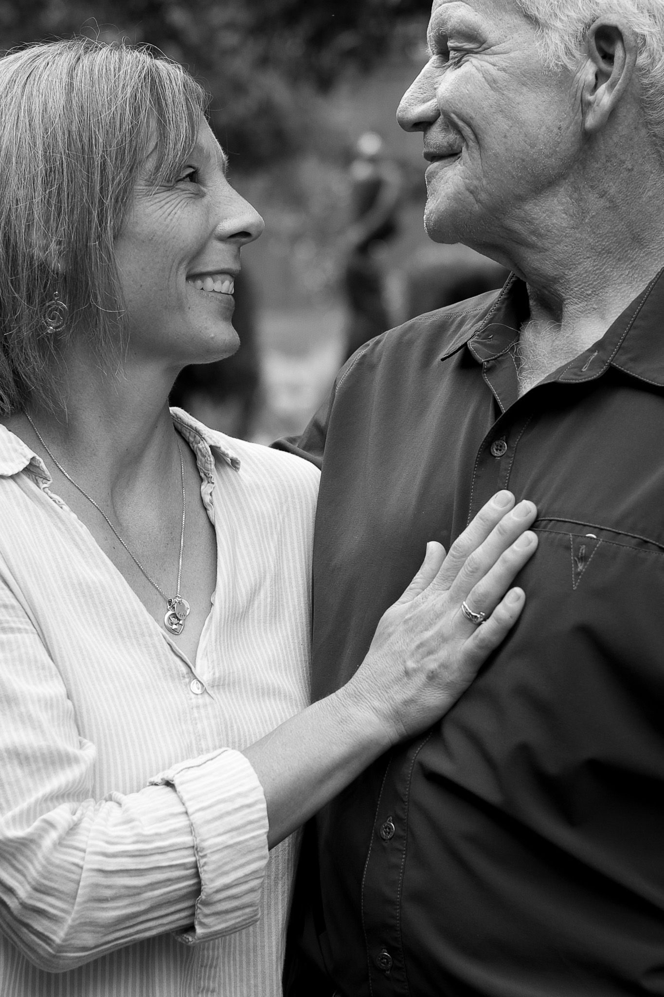 Black and white portrait of a mature couple smiling at each other in an outdoor garden setting.