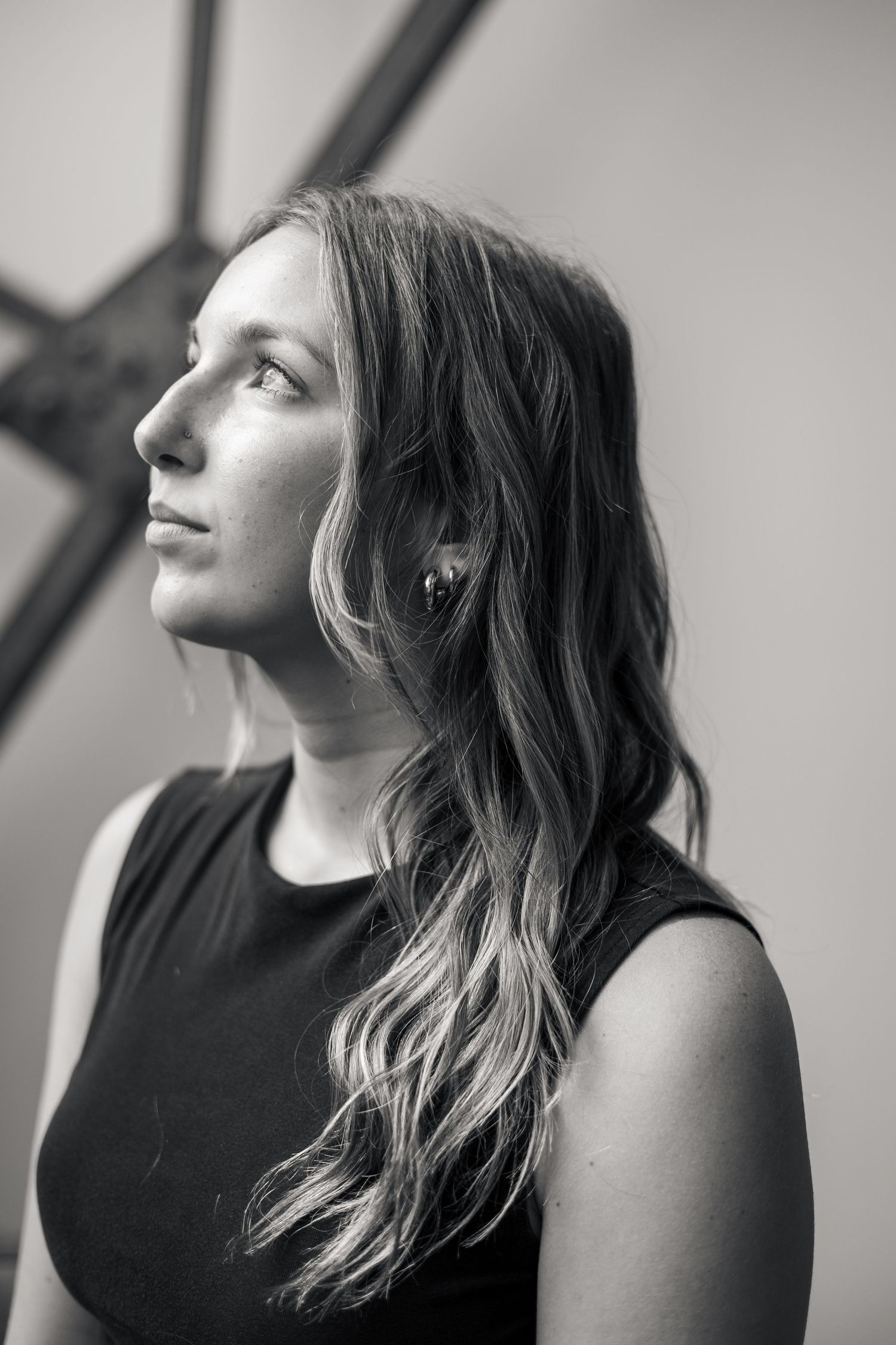 Black and white profile portrait of a young woman with long wavy hair wearing a sleeveless black top.