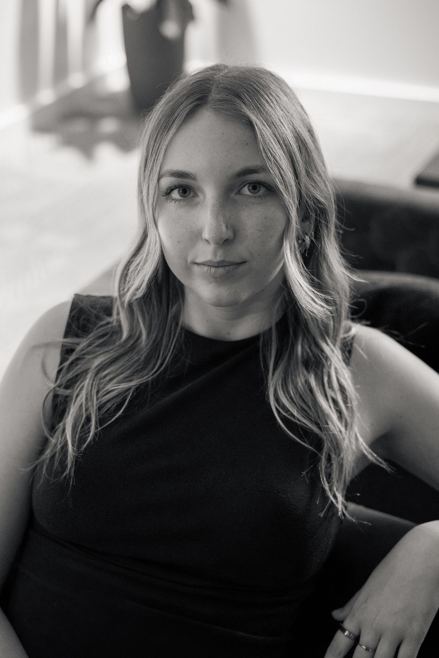 Black and white close-up portrait of a young woman with long wavy blonde hair in a black sleeveless dress.