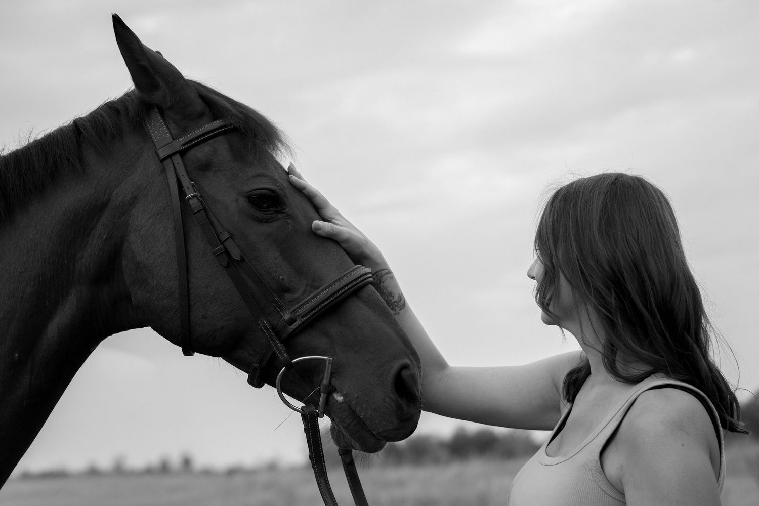 Black and white photo of a young woman gently touching a horse's nose in an open field.