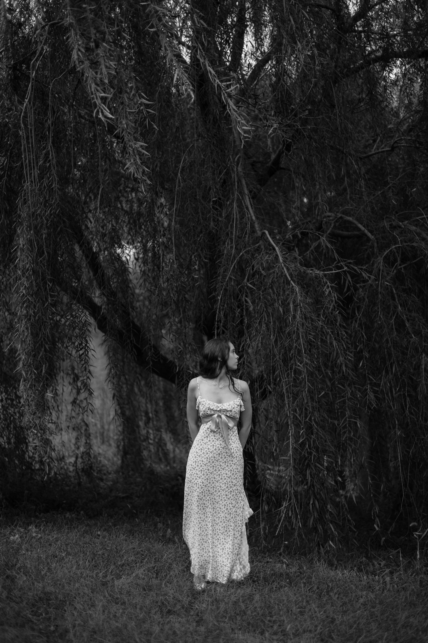 Woman in floral maxi dress standing under weeping willow tree, black and white fine art photography.