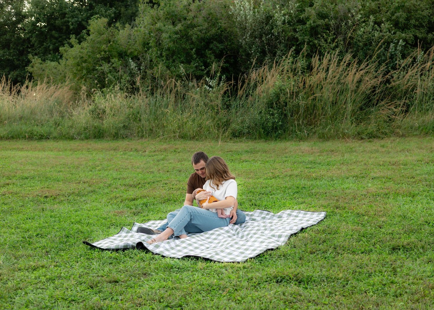 Couple sitting on a checkered blanket in a green field, enjoying a romantic outdoor picnic together.