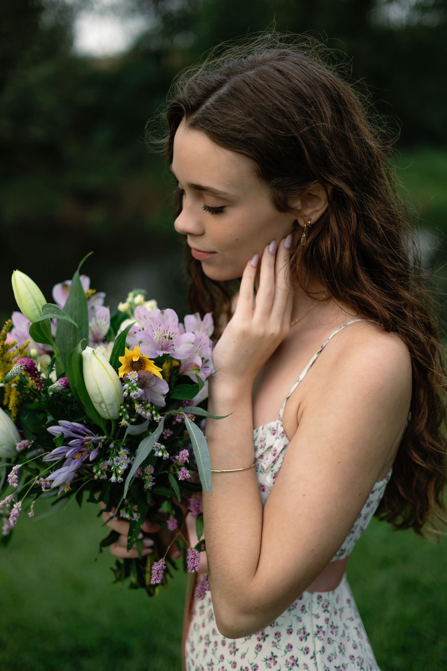 Young woman in floral dress holding a colorful bouquet of lilies and wildflowers outdoors.