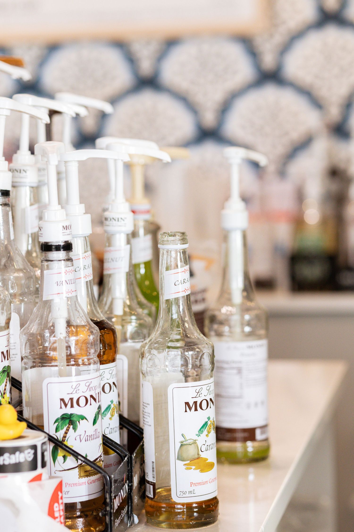 Monin flavored syrups with pump dispensers lined up on a white counter in a cafe setting.