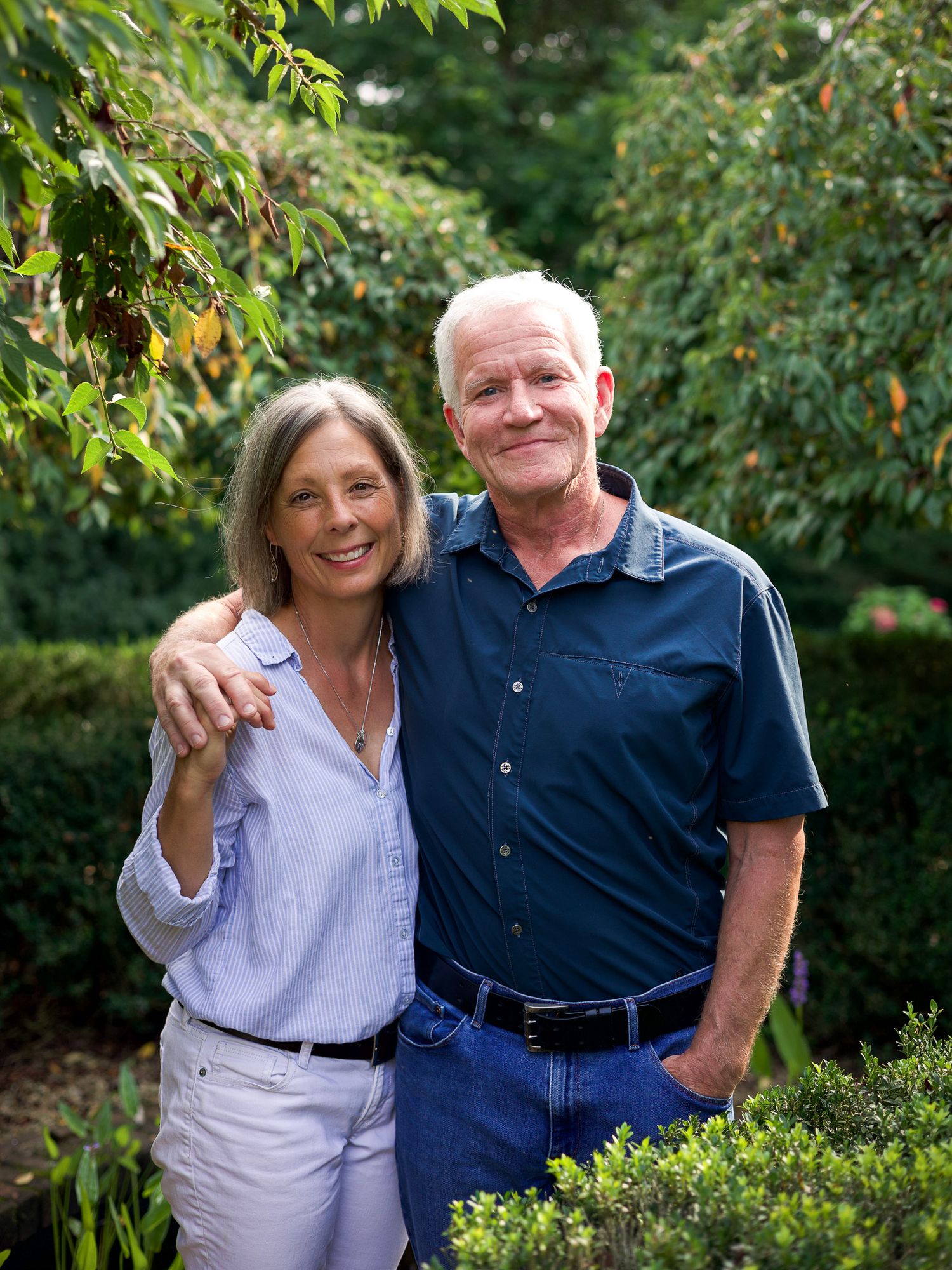 Smiling older couple embracing outdoors in a lush green garden on a sunny day.