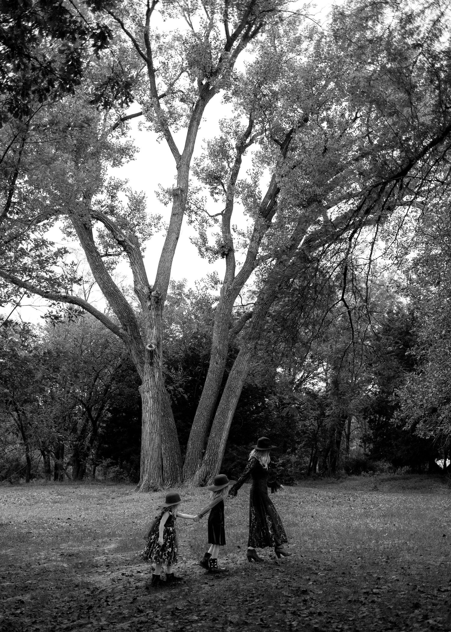 Black and white photo of children holding hands and dancing around a large tree in a park.