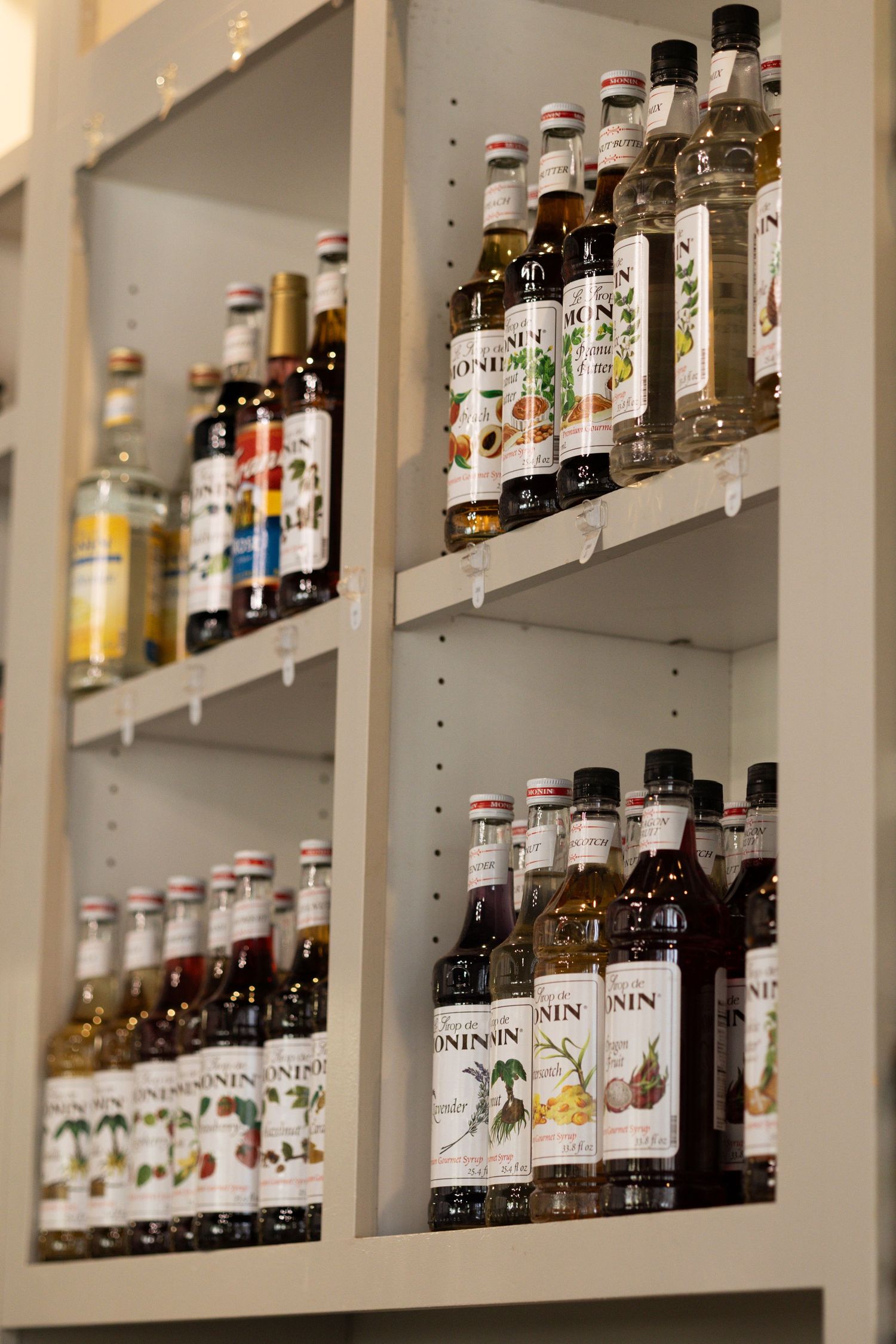 Shelves stocked with Monin flavored syrups in various bottles at a coffee shop or bar.