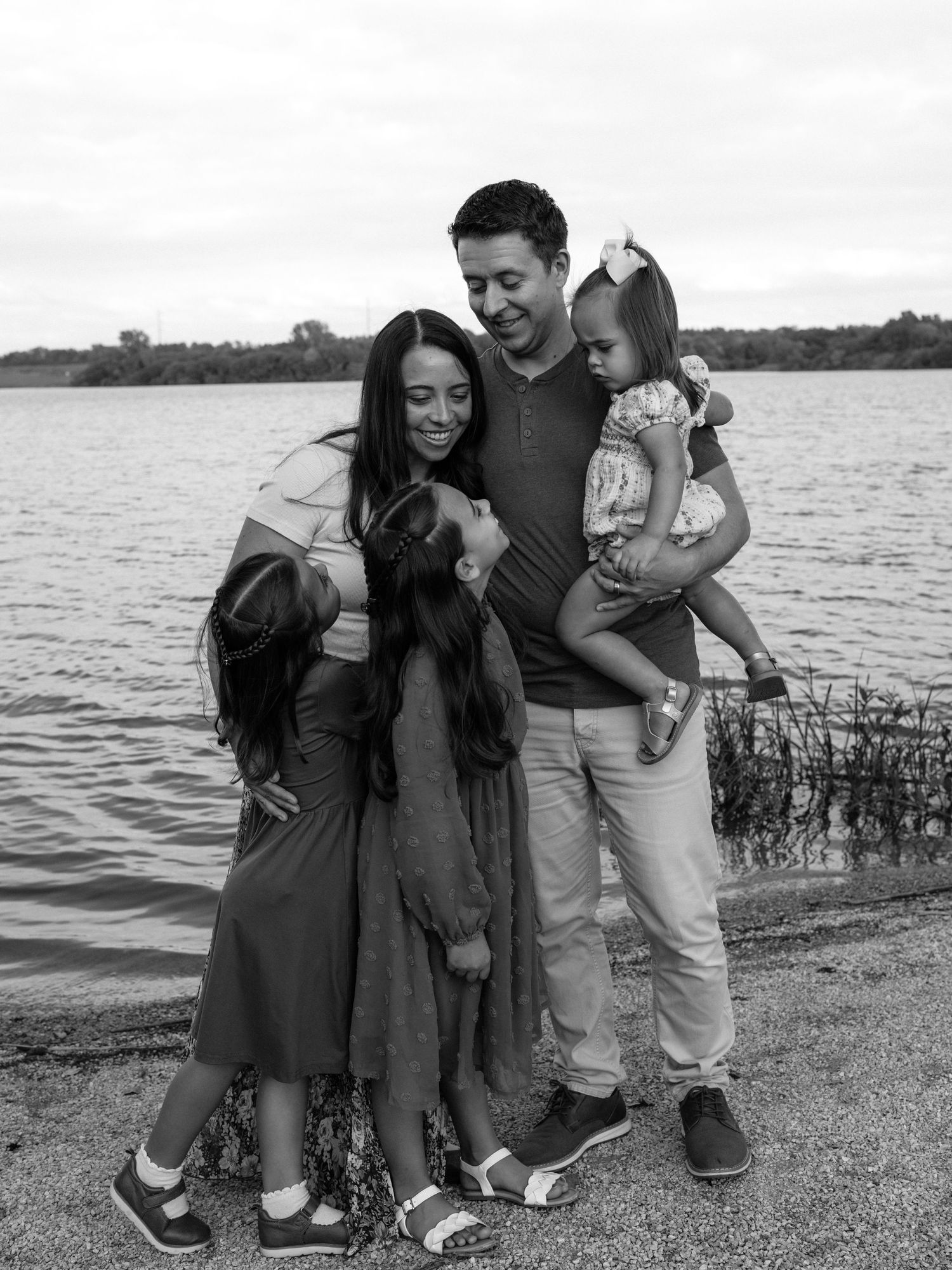 Black and white family photo of parents and two young daughters laughing together by a lakeside.