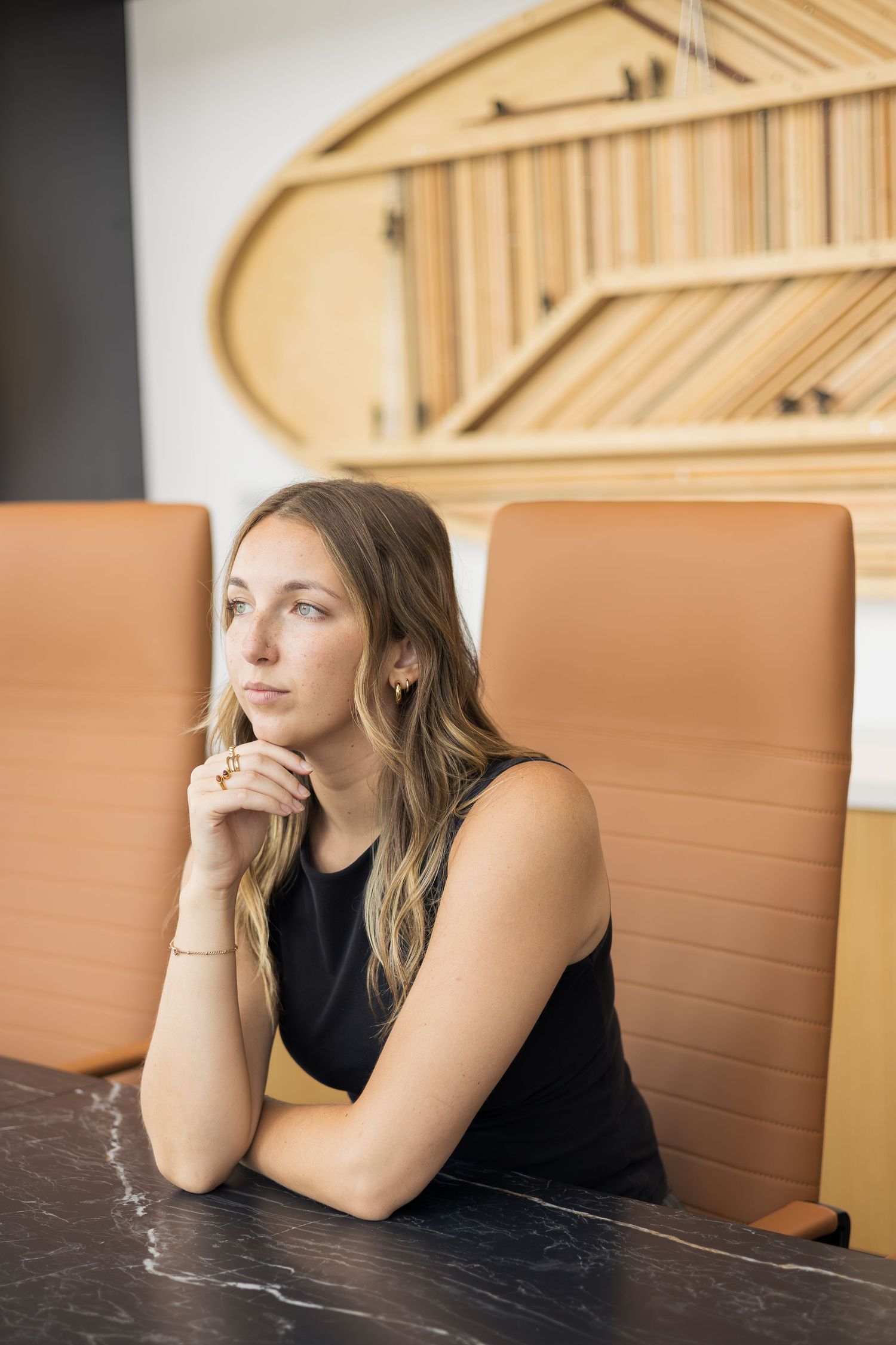 Thoughtful young woman with hands clasped sitting at a marble table in a modern office boardroom.