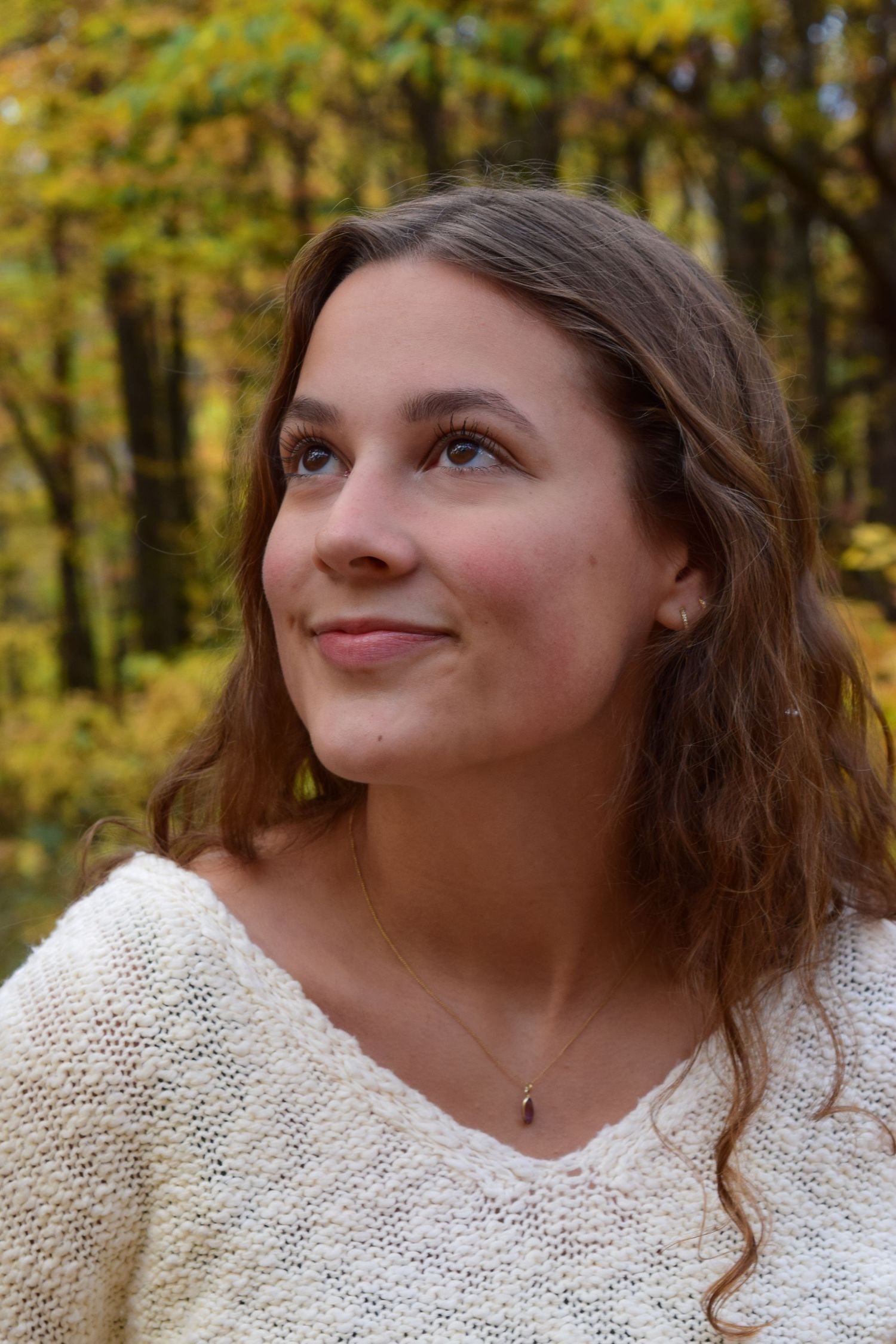 Young woman with long brown hair smiling upward in an autumn forest with golden foliage.