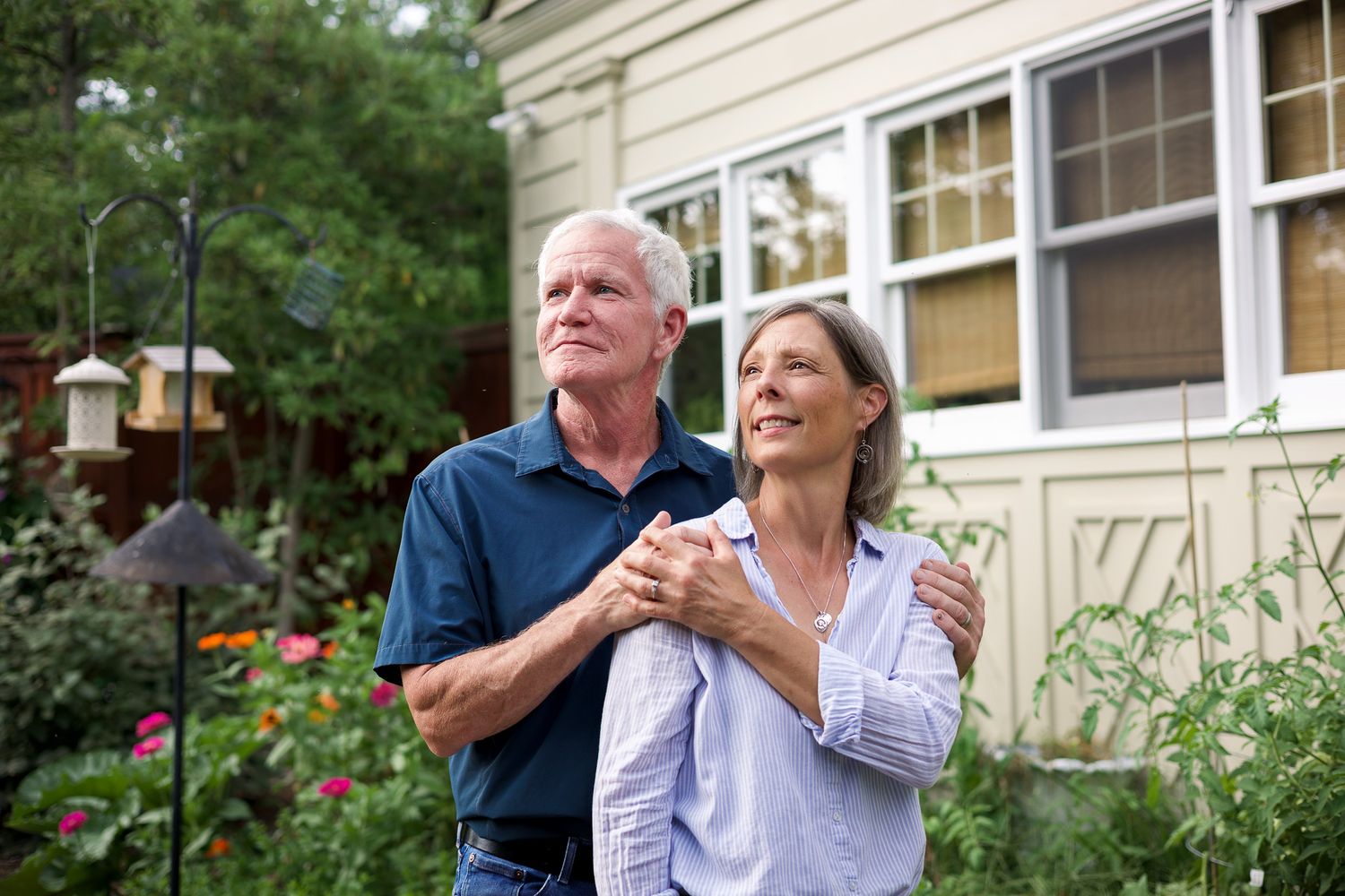 Happy senior couple embracing in backyard garden near their home, enjoying retirement together outdoors.