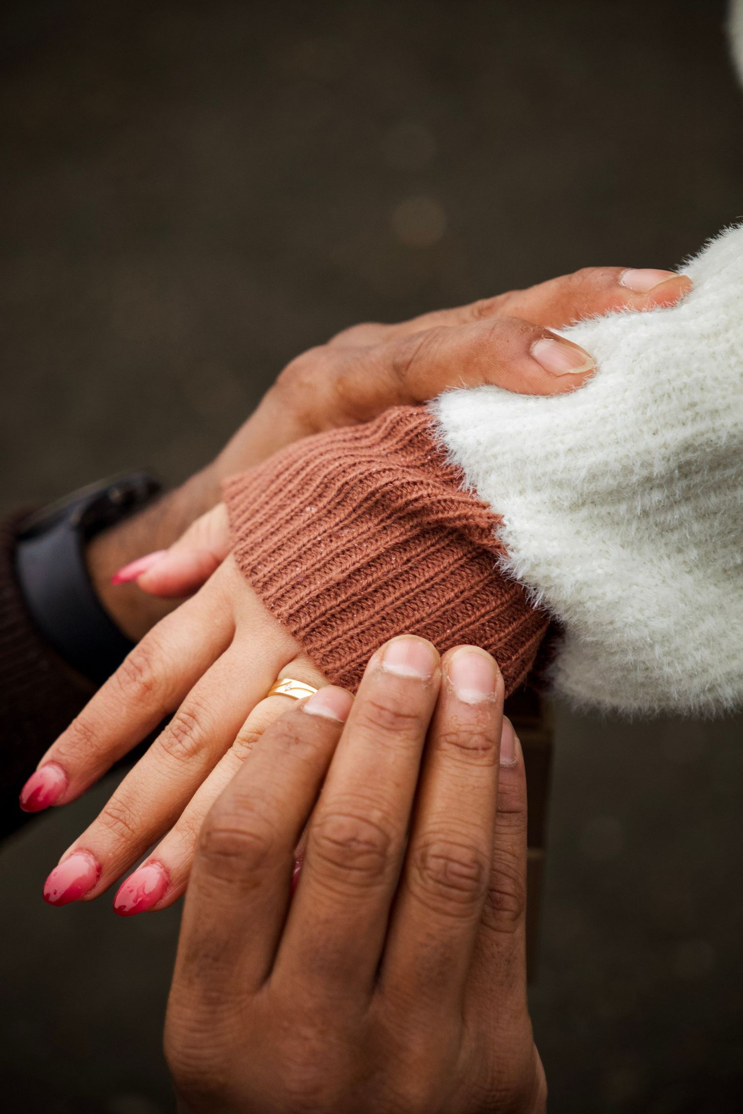 Close-up of two hands with French manicure and pink nails, wearing gold rings, resting on a cozy knit sweater sleeve.