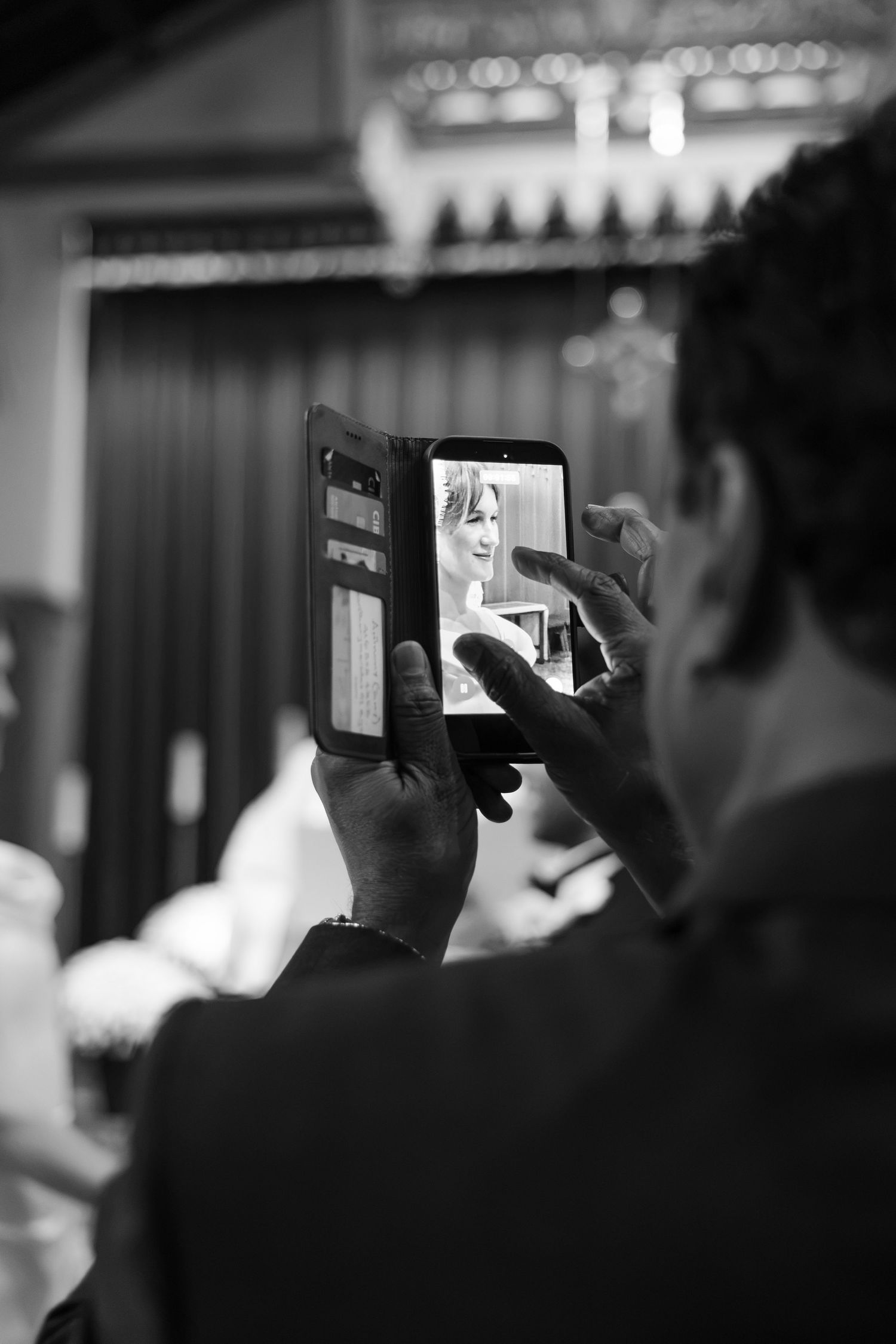 A wedding guest captures the bride on his smartphone during the ceremony in black and white.