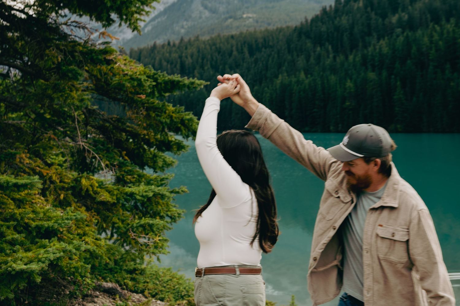 Couple dancing by a turquoise mountain lake surrounded by pine trees.
