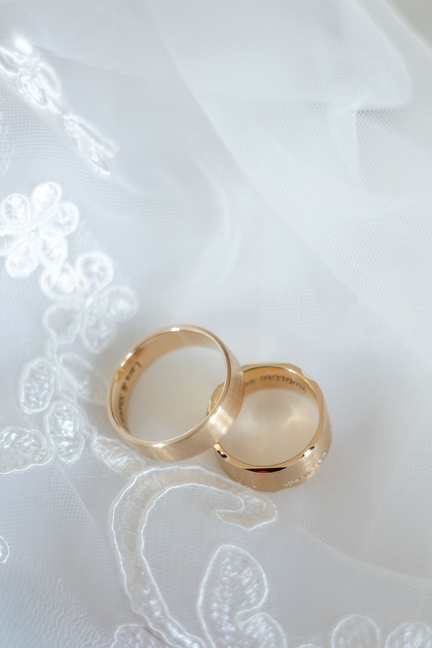 Two gold wedding bands resting on white lace bridal veil fabric.