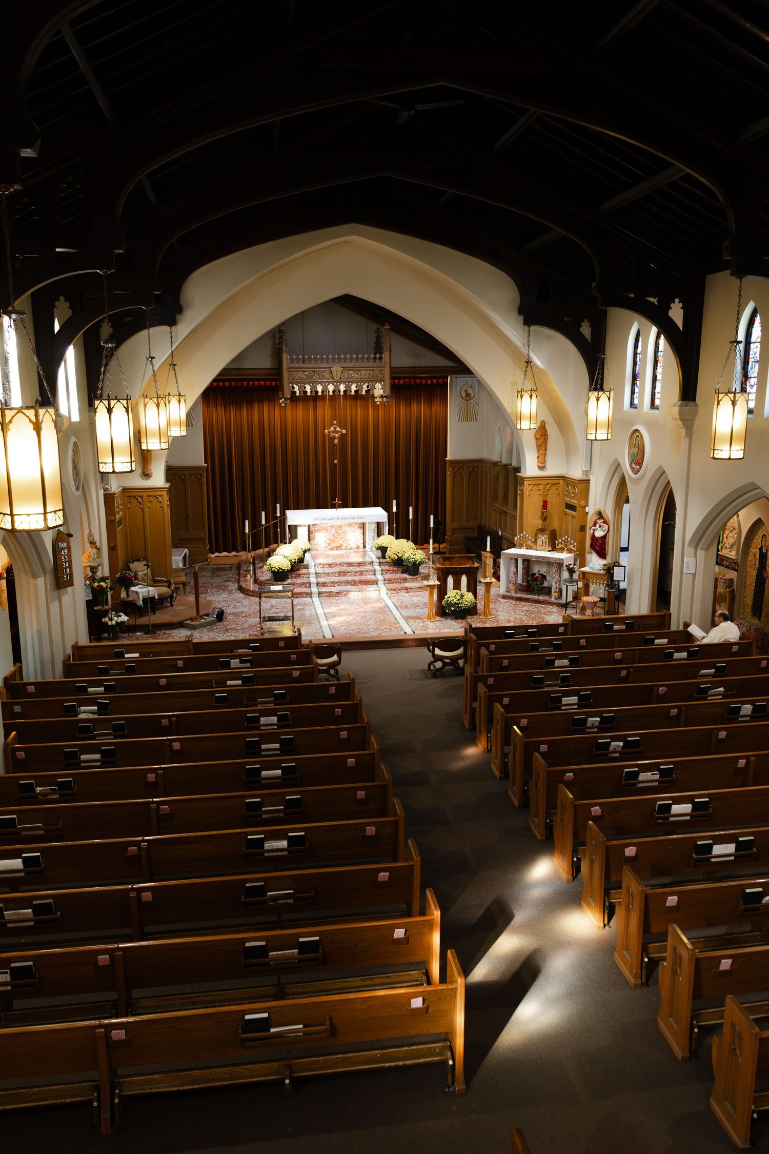 Interior view of an empty church with wooden pews, arched ceilings, and an illuminated altar with candles.