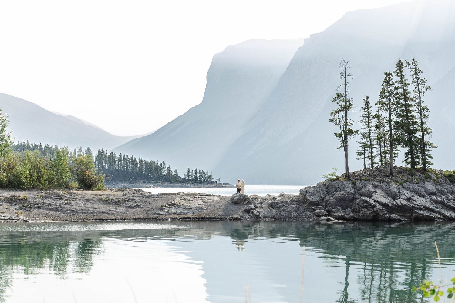 Serene mountain lake with turquoise water, rocky shoreline. Romantic couple in Minnewanka Lake in Banff.