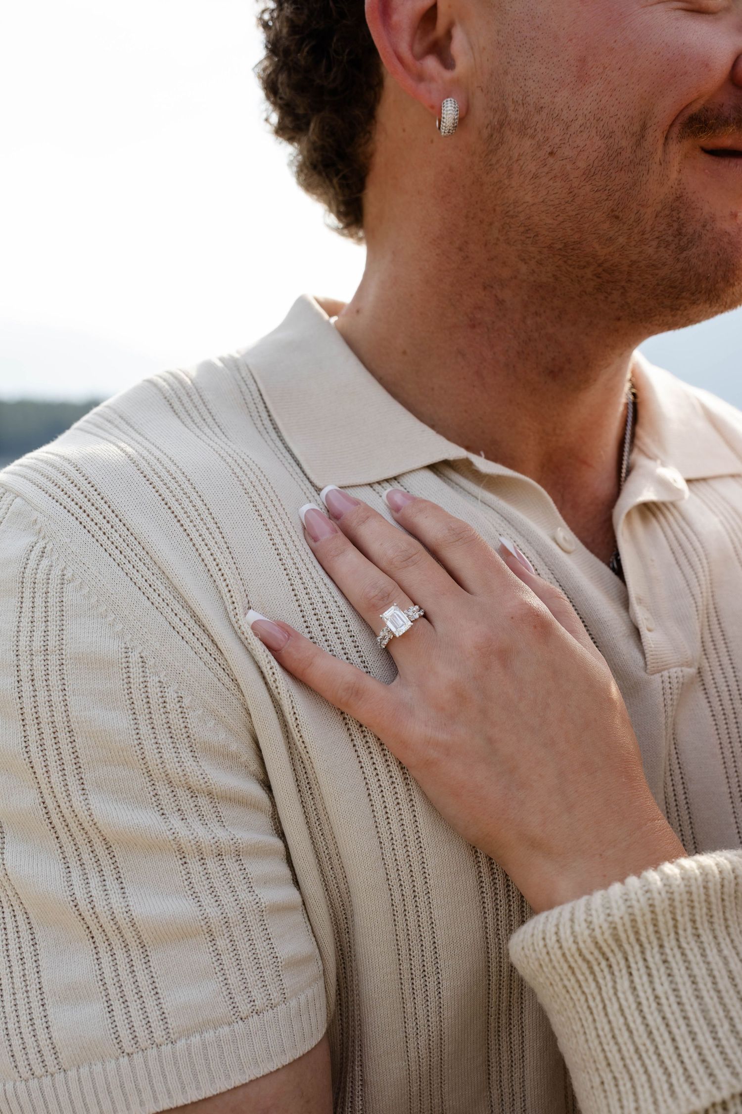 Close-up of a hand wearing a large emerald-cut diamond engagement ring resting on a man's chest.Romantic couple in Minnewanka Lake in Banff.