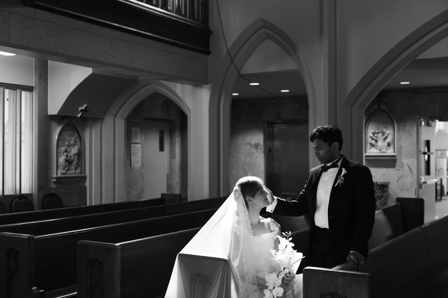 Black and white photo of a bride and groom sharing a quiet moment together inside a traditional church.