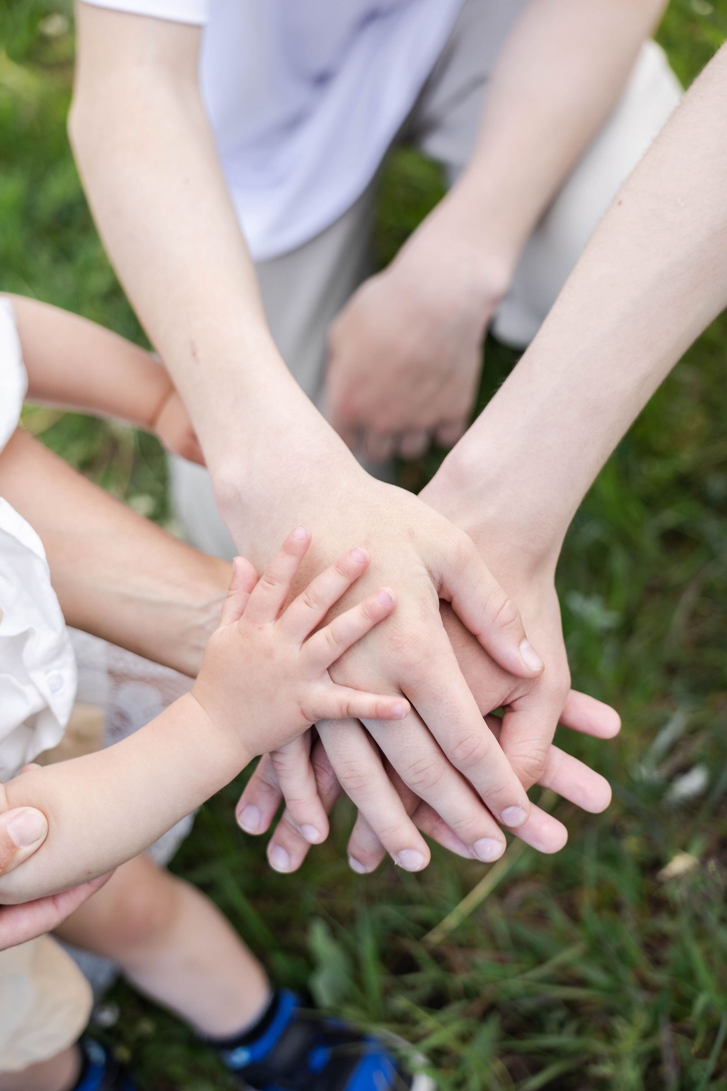 Family stacking hands together outdoors on green grass, symbolizing unity, teamwork, and togetherness.