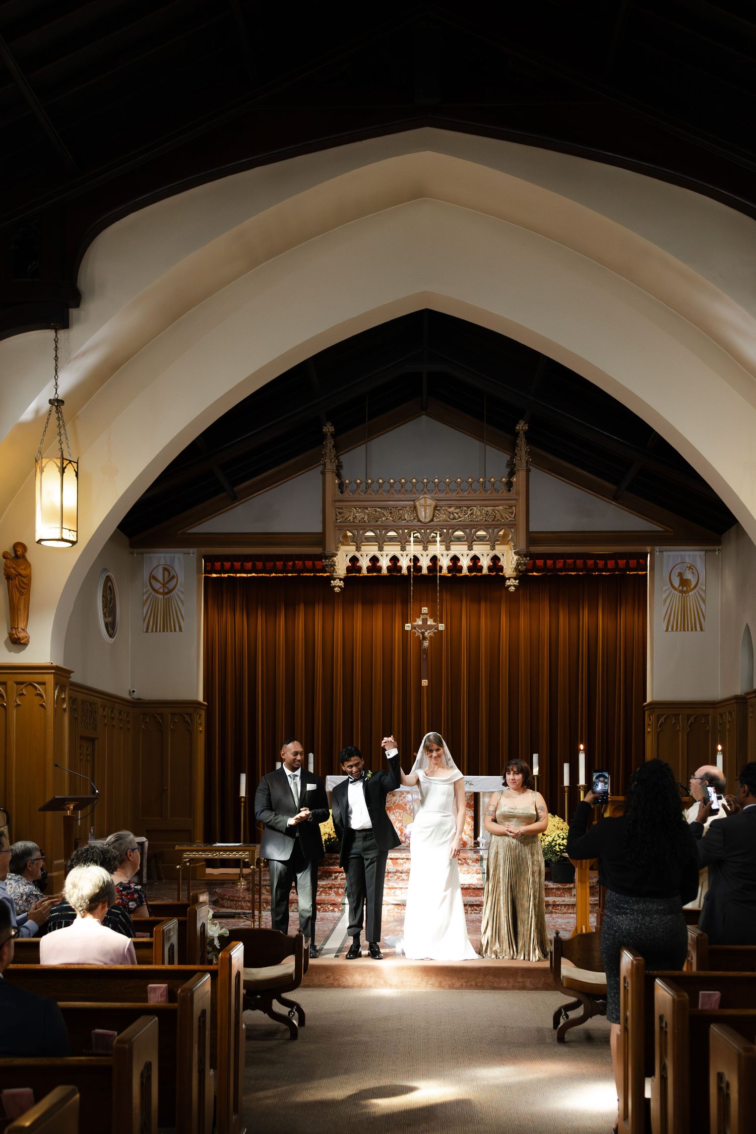 Couple exchanges vows at elegant church wedding ceremony with gothic arched ceiling and wooden altar backdrop.