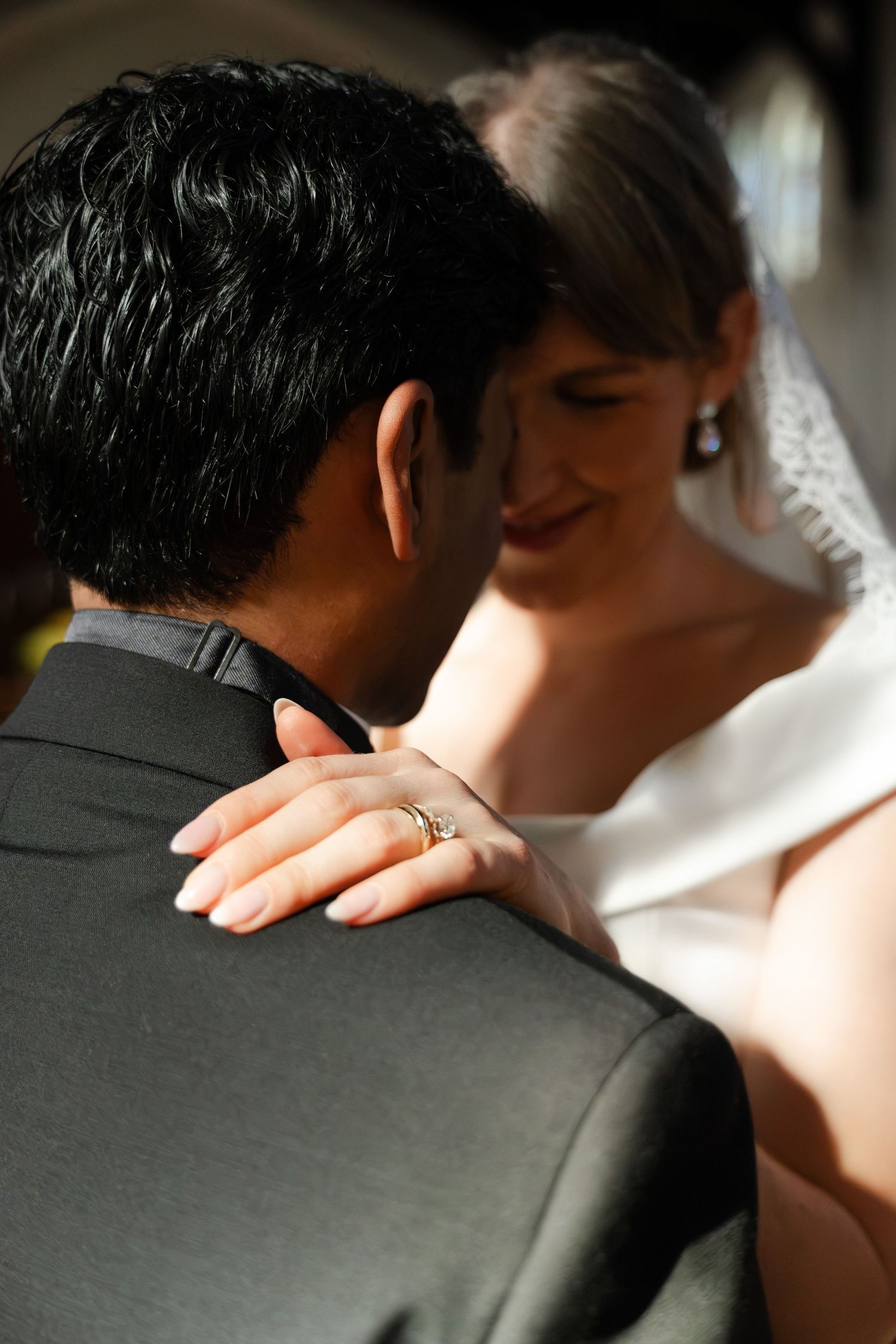 Bride in white veil places ringed hand on groom's shoulder during romantic wedding dance.