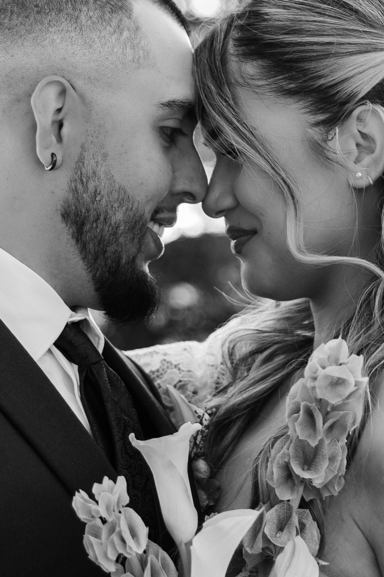 Black and white wedding photo of bride and groom touching foreheads, smiling intimately, with floral details.