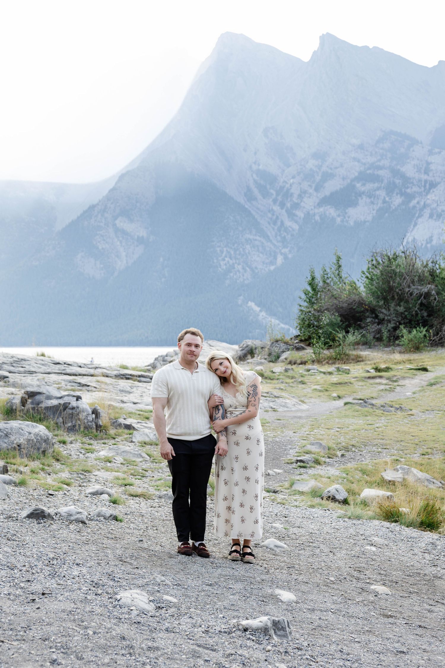 Couple posing on rocky mountain lakeshore path with dramatic misty peaks in the background.Romantic couple in Minnewanka Lake in Banff.